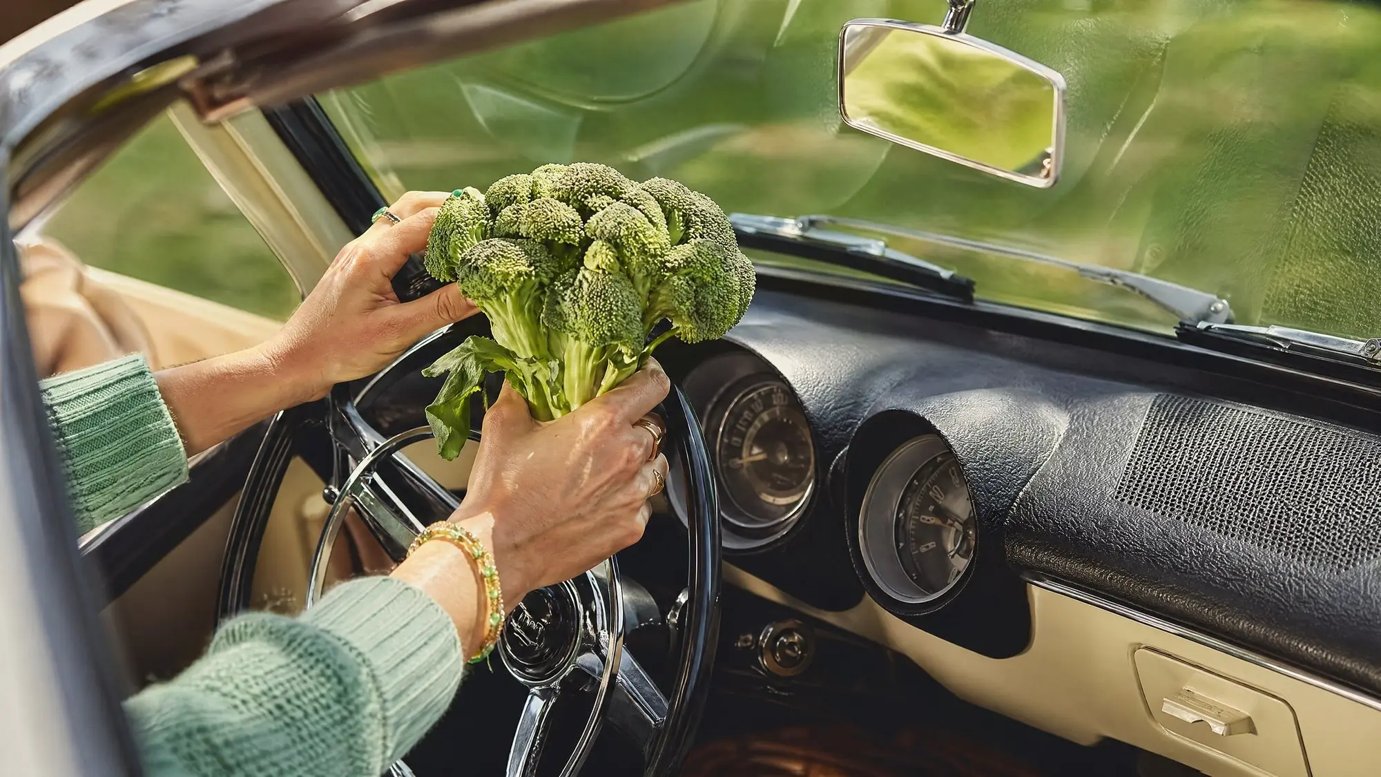 Manos sujetando un brócoli dentro de un coche clásico
